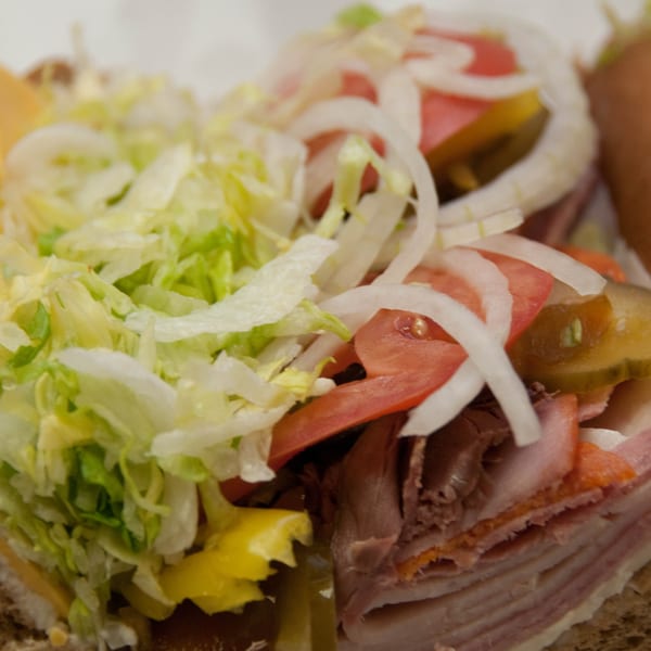 Close-up of a Mr. Submarine & Salads sandwich, piled high with lettuce, onions, tomatoes, and deli meats.