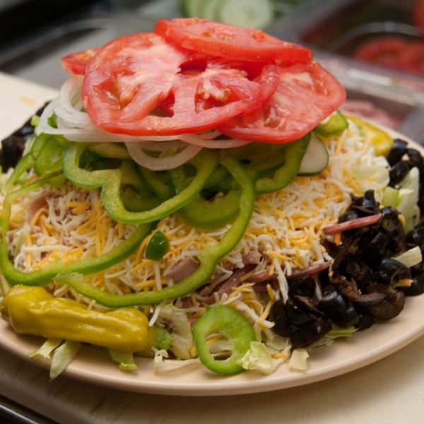 A large salad from Mr. Submarine & Salads, topped with tomatoes, onions, peppers, cheese, and olives.