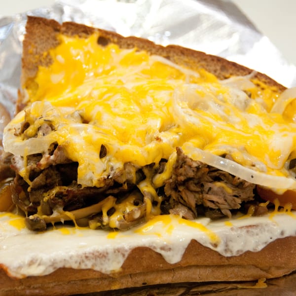 Close-up of a Mr. Submarine & Salads cheesesteak sandwich with melted cheese, steak, and onions.
