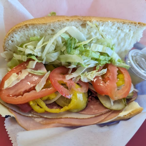 A Mr. Submarine & Salads sandwich, filled with deli meats, cheese, lettuce, tomatoes, and pickles.