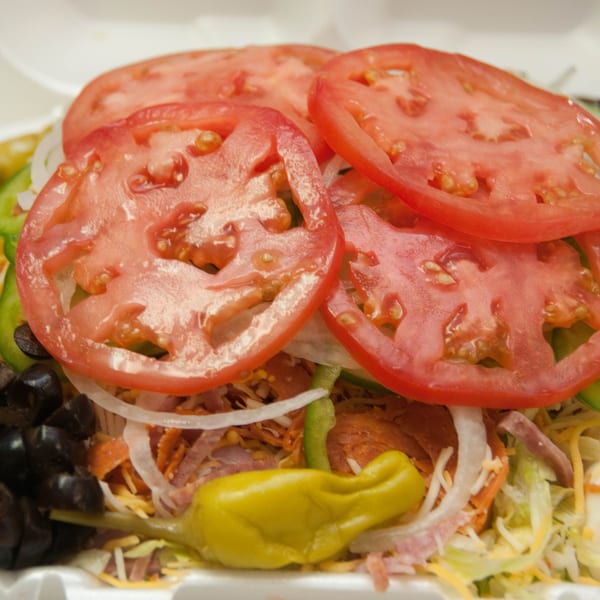 Close-up of a Mr. Submarine & Salads sandwich with sliced tomatoes, onions, olives, and peppers.